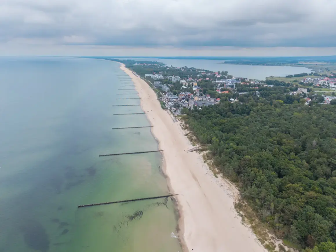 Widok z lotu ptaka na plażę w Mielnie, z falochronami i lasem sosnowym. To jedne z wielu atrakcji w Mielnie.