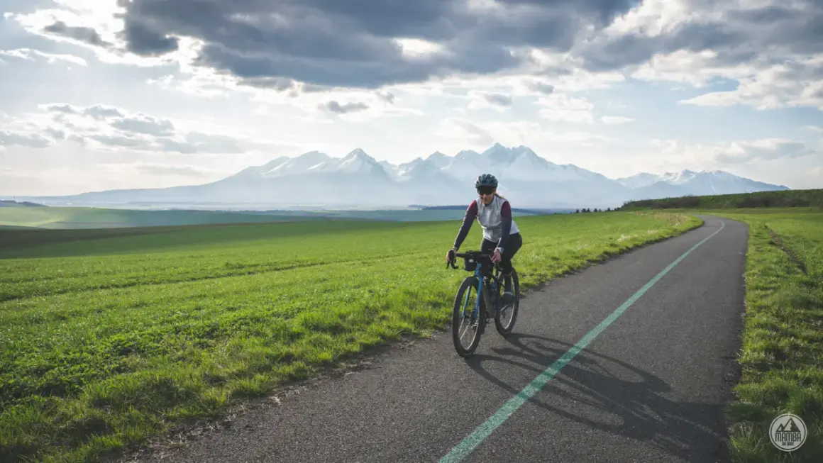 Kobieta na rowerze pokonuje malowniczą trasę z widokiem na ośnieżone Tatry. To wyzwanie: rowerem dookoła Tatr w jeden dzień!