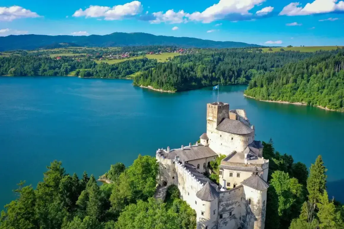 Zamek w Niedzicy góruje nad turkusowym zalewem czorsztyńskim, otoczony zielonymi lasami i pagórkami.