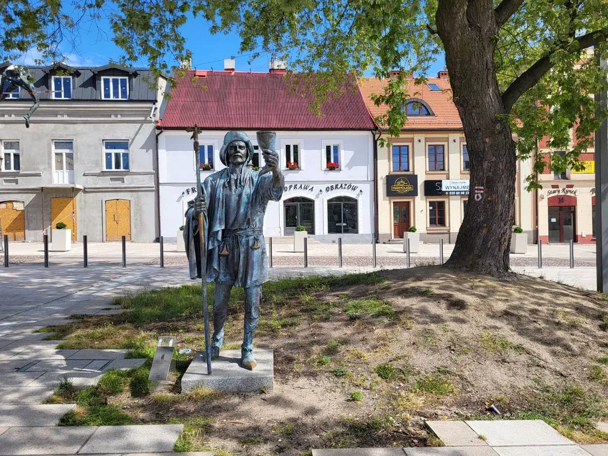 Pomnik pielgrzyma z kielichem i laską, jedna z częstochowskich atrakcji, na tle kolorowych kamienic.