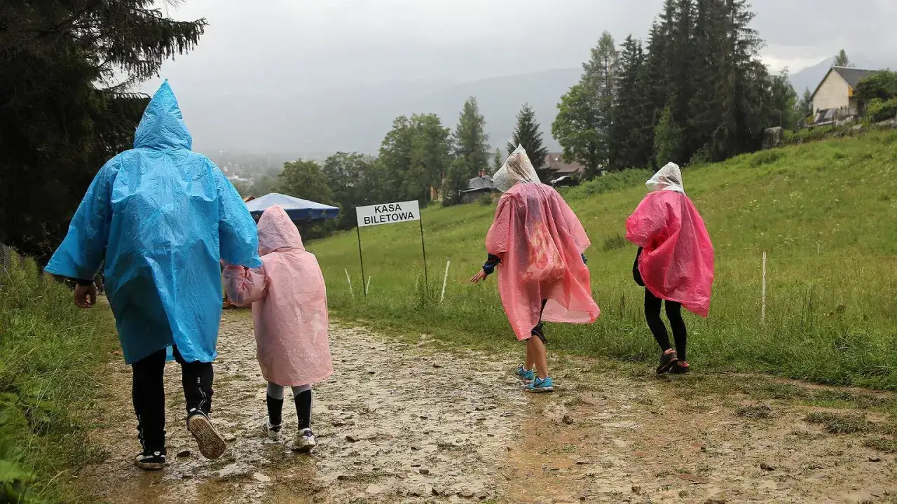 Rodzina w kolorowych pelerynach idzie błotnistą ścieżką. Nawet gdy pada deszcz, można znaleźć ciekawe rzeczy do robienia w Zakopanem, np. spacer do kasy biletowej.
