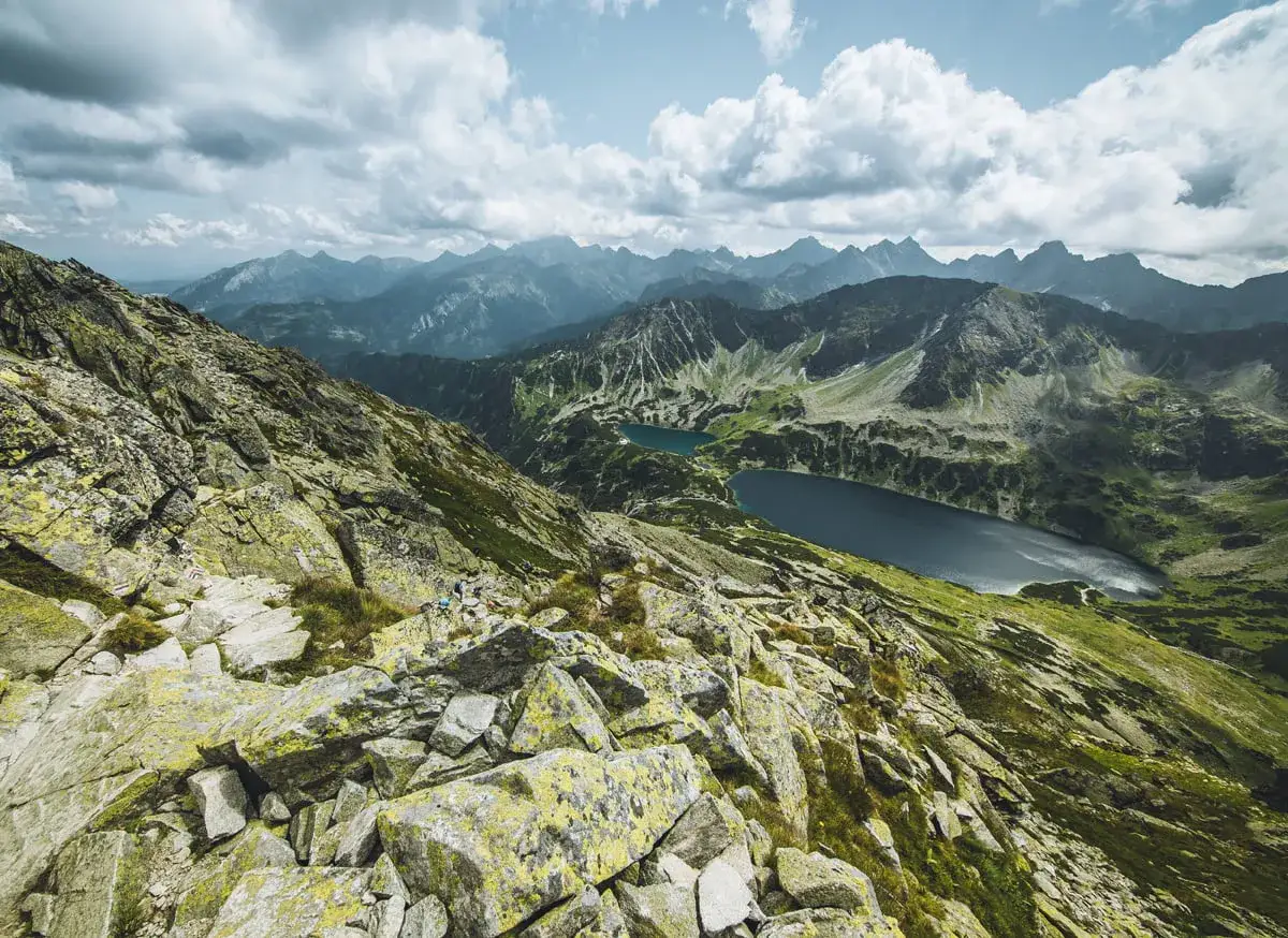 Widok z Kozi Wierch na Tatry. Dwa jeziora w dolinie, skaliste zbocza, chmury na niebie.