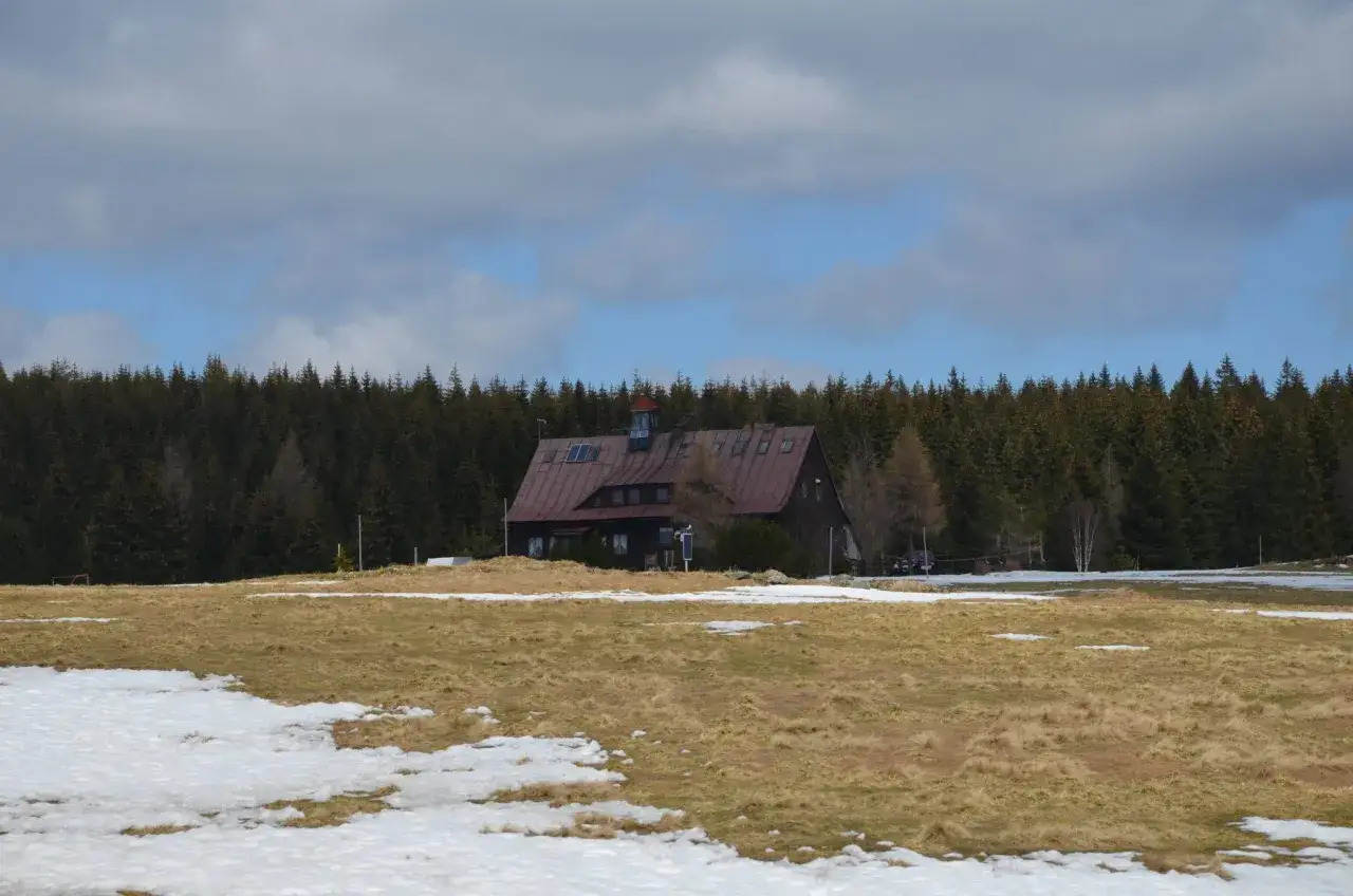 Dom w g&oacute;rach izerskich, otoczony lasem i polami ze śniegiem.