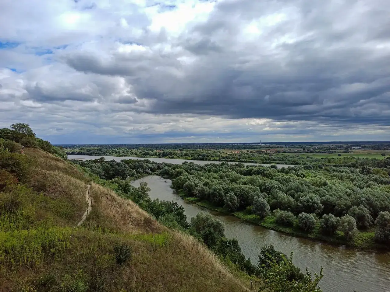 Widok z g&oacute;r pieprzowych na meandrującą rzekę otoczoną zielenią. Chmury na niebie zapowiadają deszcz.