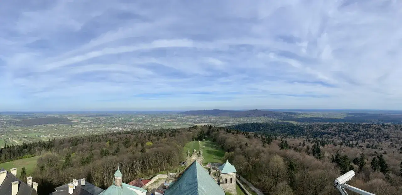 Widok z Łysej Góry na rozległą dolinę i pagórkowaty krajobraz. Na pierwszym planie fragmenty budowli sakralnych.