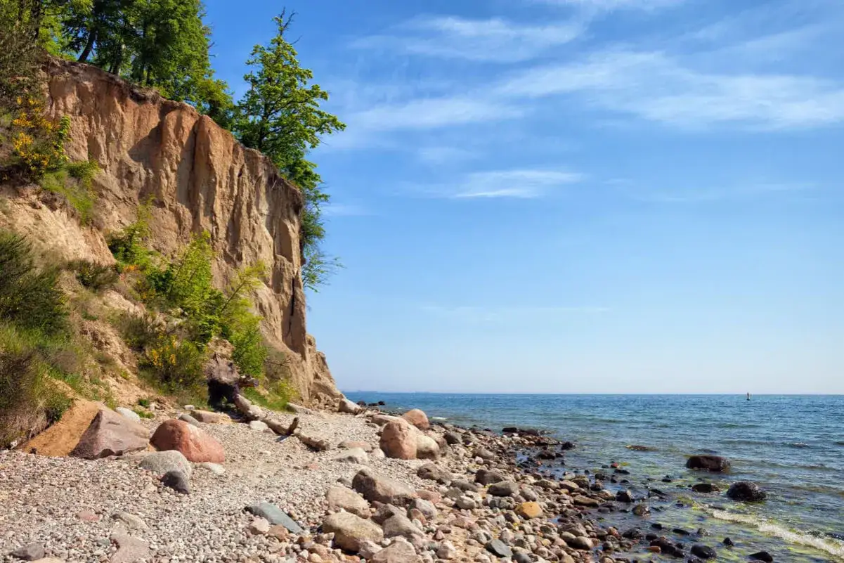 Wysokie, piaszczyste klify w Polsce porośnięte zielenią, z kamienistą plażą i spokojnym morzem pod błękitnym niebem.