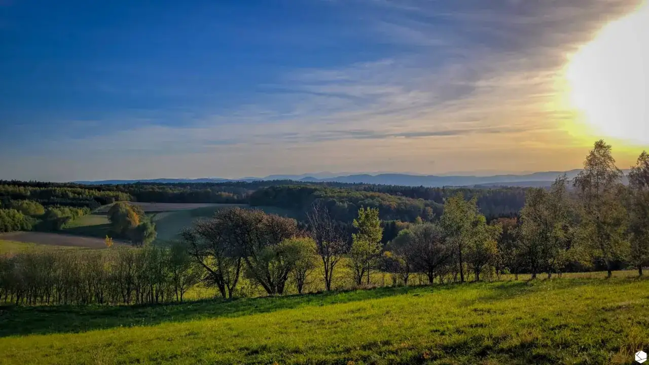 Zach&oacute;d słońca nad G&oacute;rami Kaczawskimi. Zielone wzg&oacute;rza, lasy i łagodne pasma g&oacute;rskie w oddali.