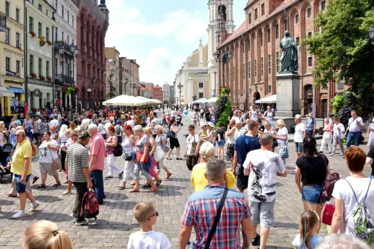 Tłum ludzi na brukowanym rynku, z zabytkowymi kamienicami i pomnikiem. Czy to bydgoszcz czy toruń?