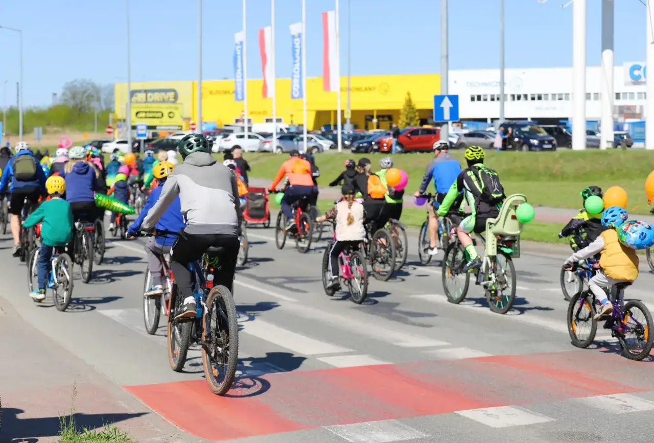 Rowerzyści na ulicy, część peletonu na trasach rowerowych Kujawsko-Pomorskiego. Dzieci i dorośli w kaskach, słońce.