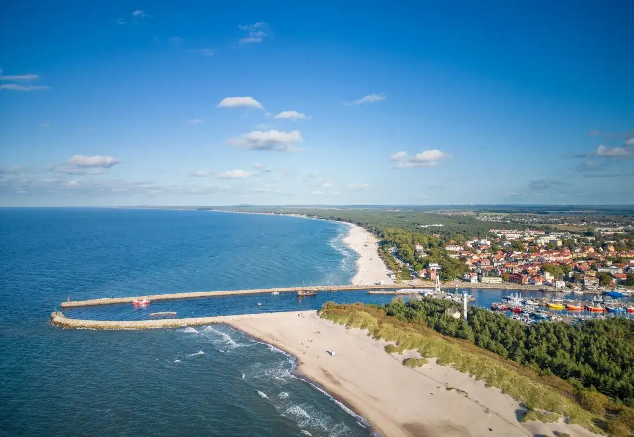 Widok na port i plażę w Ustce. Widać falochrony, morze, piaszczyste plaże, las i zabudowania miejskie. To idealne miejsce na odkrywanie atrakcji Ustki i okolic.