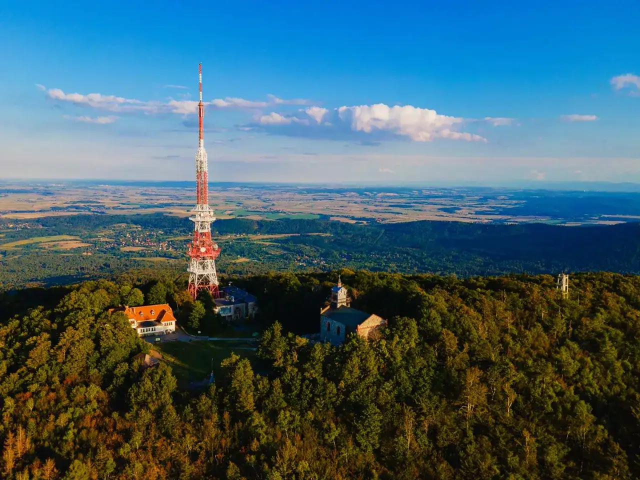 Wieża telekomunikacyjna na g&oacute;rze Ślęża g&oacute;ruje nad lasami i polami. Widać też budynki i kości&oacute;łek.