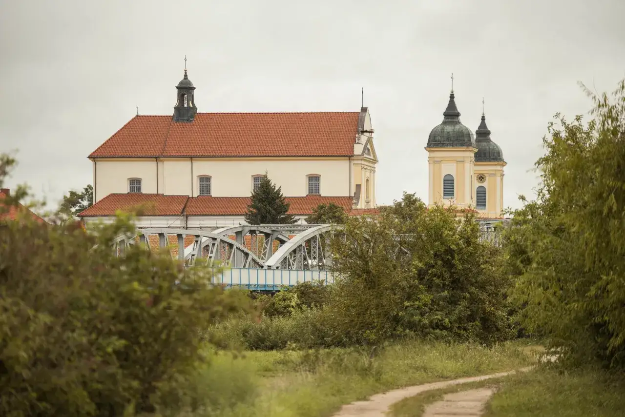 Malownicza trasa w Tykocinie prowadzi przez zielone tereny, w oddali widać zabytkowe kościoły i most.