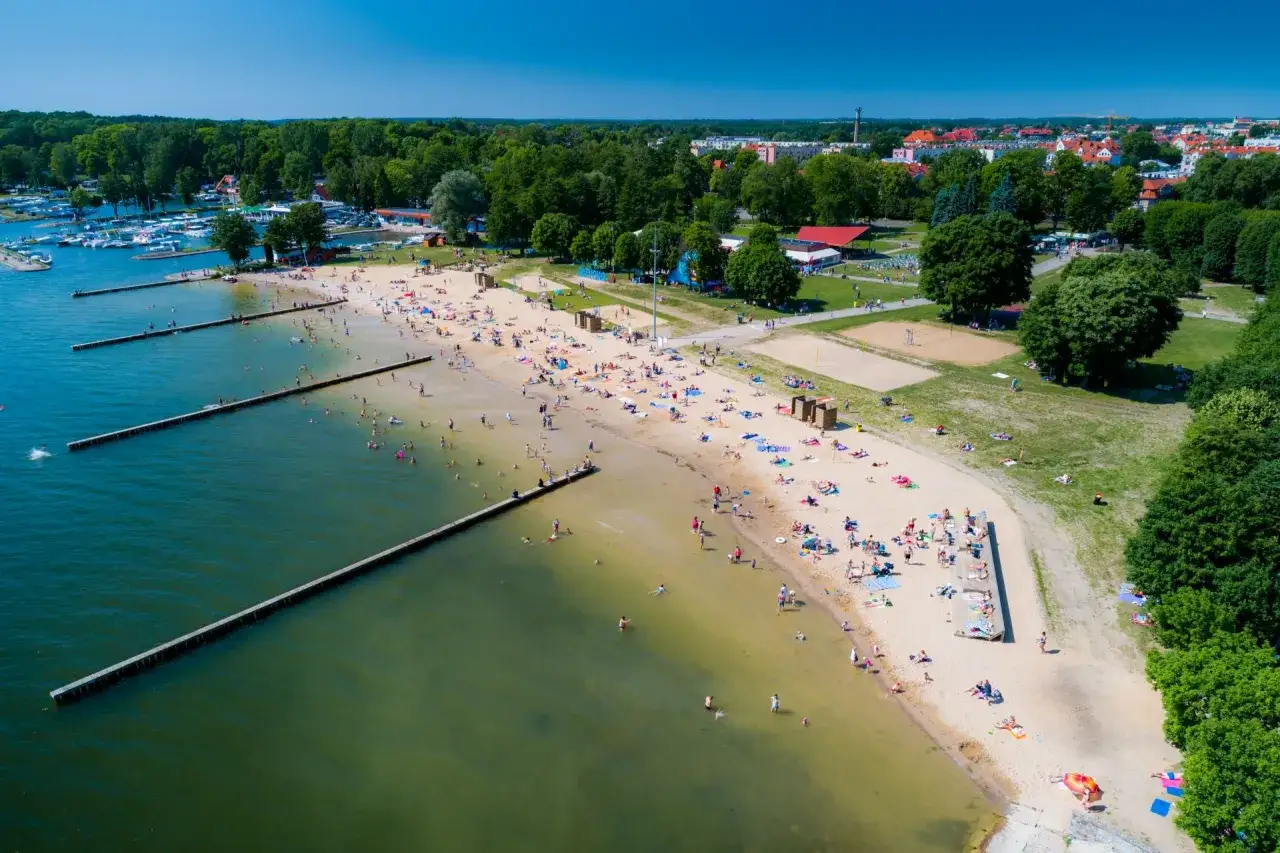 Słoneczny dzień na plaży w Giżycku. Tłumy ludzi kąpią się i opalają, korzystając z urok&oacute;w Mazur. To idealne giżycko atrakcje dla każdego.