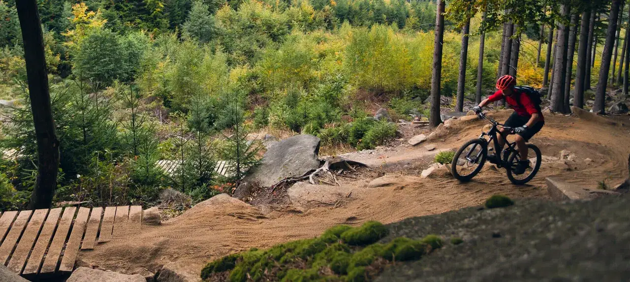 Rowerzysta w kasku pokonuje zakręt na piaszczystej, fortecznej trasie rowerowej w lesie.