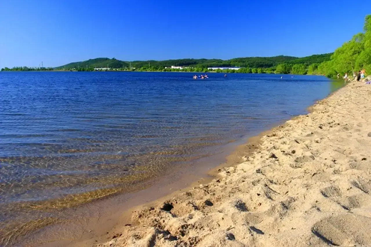 Słoneczny dzień nad Zalewem Sulejowskim. Piękna plaża, błękitna woda i zielone wzg&oacute;rza w tle. Idealne miejsce na wypoczynek i odkrywanie atrakcji.
