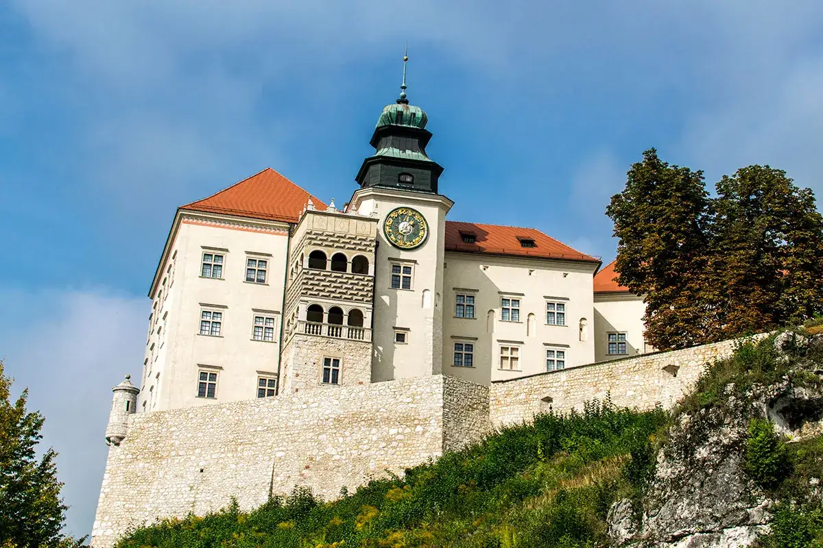 Zamek na skale, jakby zbudowany przez Herkulesa, z wieżą zegarową i kamiennymi murami.
