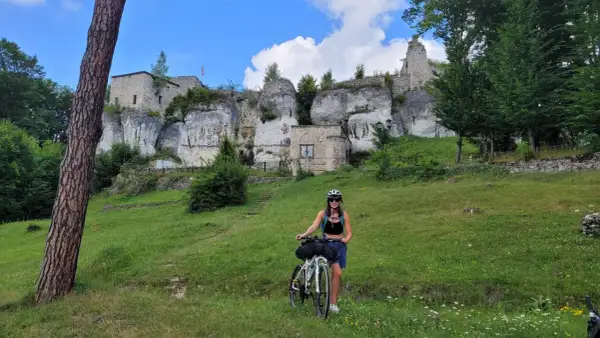 Kobieta z rowerem na tle ruin zamku na skale. Piękny dzień na odkrywanie szlak orlich gniazd rowerem.