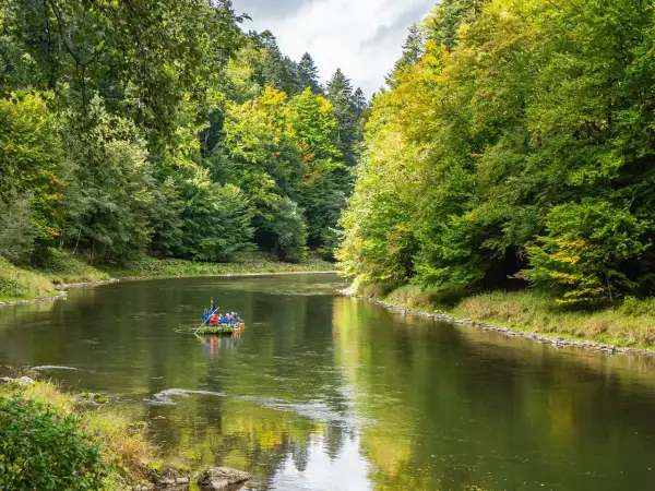 Spływ Dunajcem w Pieninach. Tratwa z turystami płynie spokojną rzeką otoczoną zielonymi lasami.