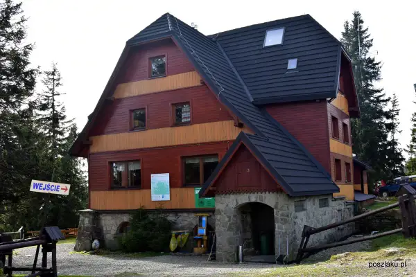 Drewniany budynek schroniska Hala Rysianka z kamiennym wejściem i znakiem "WEJŚCIE".