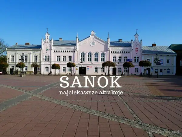 Rynek w Sanoku z pastelowymi kamieniczkami i napisem "Sanok najciekawsze atrakcje". Idealne miejsce na odkrywanie atrakcji Sanoka i okolic.
