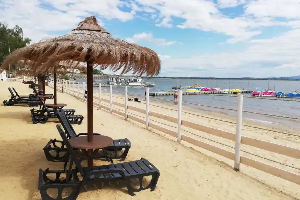 Plaża nad Jeziorem Nyskim z leżakami i parasolami. W oddali widać wodne atrakcje: łódki i rowery wodne.