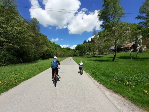 Dwie osoby na rowerach przemierzają malownicze **ojcowskie park narodowy trasy rowerowe**. Słoneczny dzień, zieleń i chmury tworzą piękną scenerię.