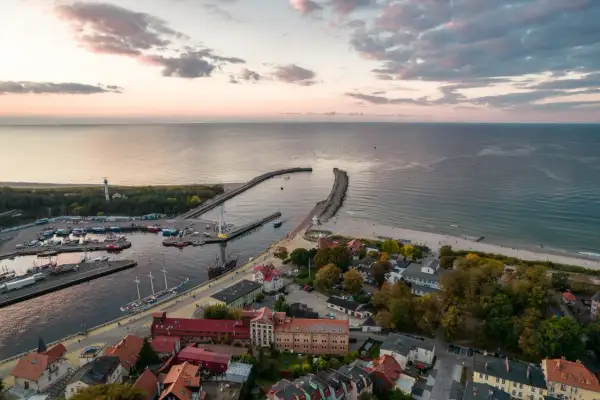 Widok na port i plażę w Ustce. Widać łodzie, latarnię morską i falochrony. To idealne miejsce na odkrywanie atrakcji Ustki i okolic.