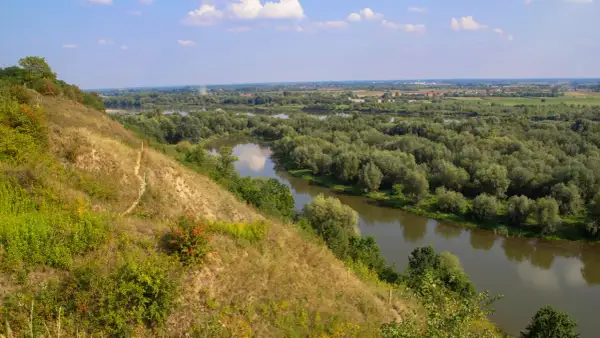 Widok na meandrującą rzekę wśród bujnej zieleni. Na pierwszym planie strome, trawiaste zbocze, przypominające krajobraz gór pieprzowych.