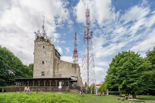 Kamienna wieża i maszty telekomunikacyjne na **chełmiec szczyt**. Ludzie odpoczywają na trawie pod drzewami.