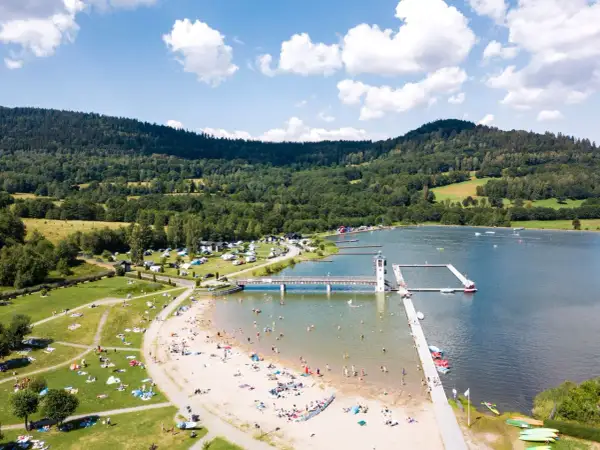 Słoneczny dzień nad zalewem Stara Morawa. Ludzie odpoczywają na plaży i w wodzie, a w tle widać zielone wzgórza.